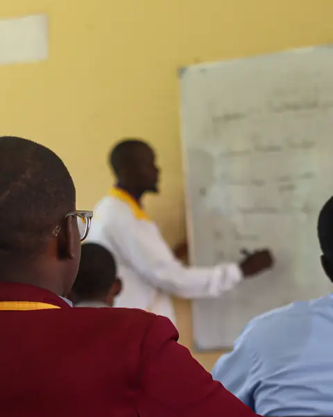 A teacher writing on a whiteboard in front of senior students