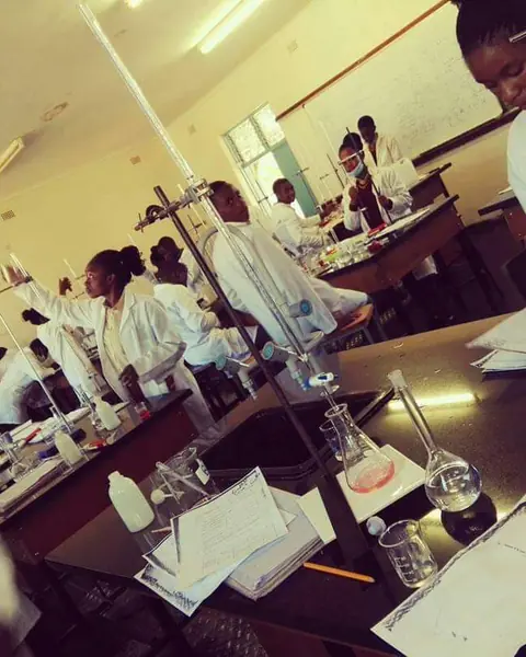 Students in white lab coats carrying out experiments in a chemistry laboratory